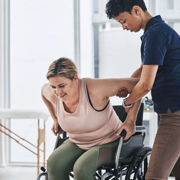 A person assists another in a wheelchair to stand up.