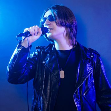 A person singing into a microphone wearing a black leather jacket.