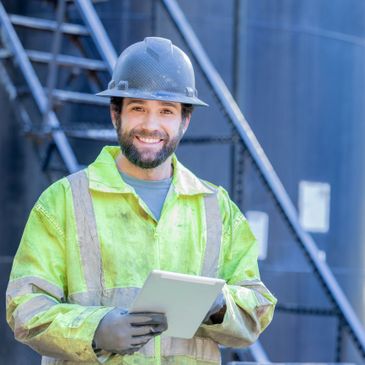 Smiling construction worker holding a tablet at a worksite.