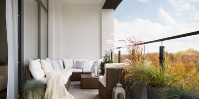 Cozy balcony with white cushioned seating and potted plants overlooking autumn trees.