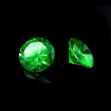Two brilliant green gemstones on a black background.