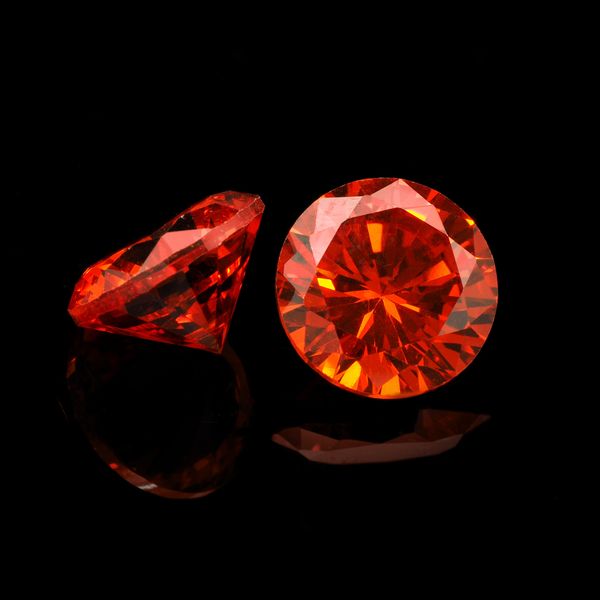 Two vibrant orange gemstones on a reflective black surface.