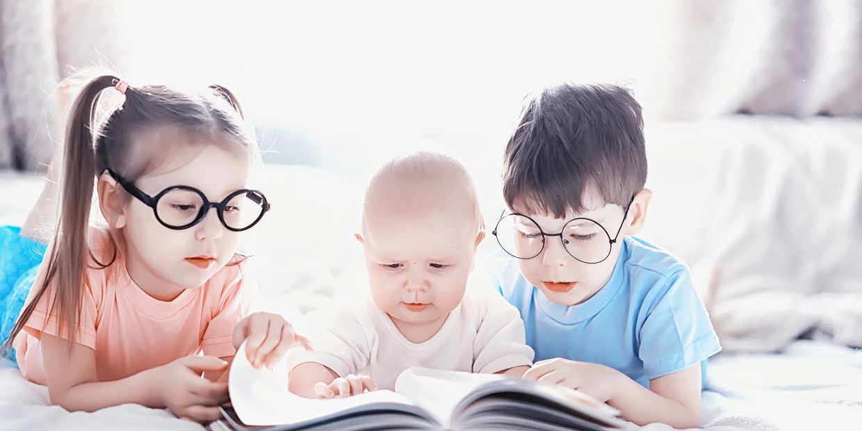 Three children reading a book together, two wearing glasses.