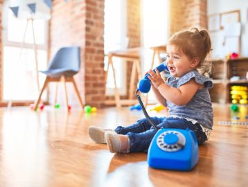 A happy toddler playing with a blue rotary phone indoors.