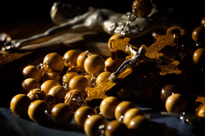 Jesus Christ catholic crucifix and wooden rosary beads under beam of light.