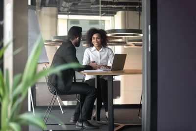 Two colleagues having a discussion at a table in a modern office.