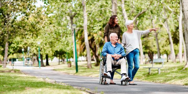 Three people enjoying a walk in a green park, with one in a wheelchair.