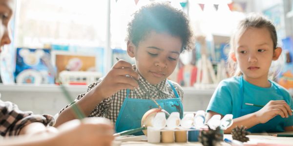 Children painting and crafting art in a bright, cheerful classroom.