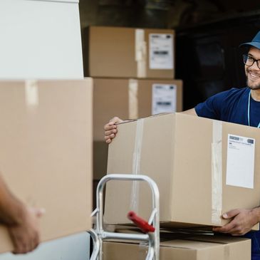 Two delivery workers carrying cardboard boxes near a van.