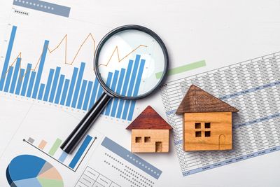 Wooden house models with financial charts and a magnifying glass.