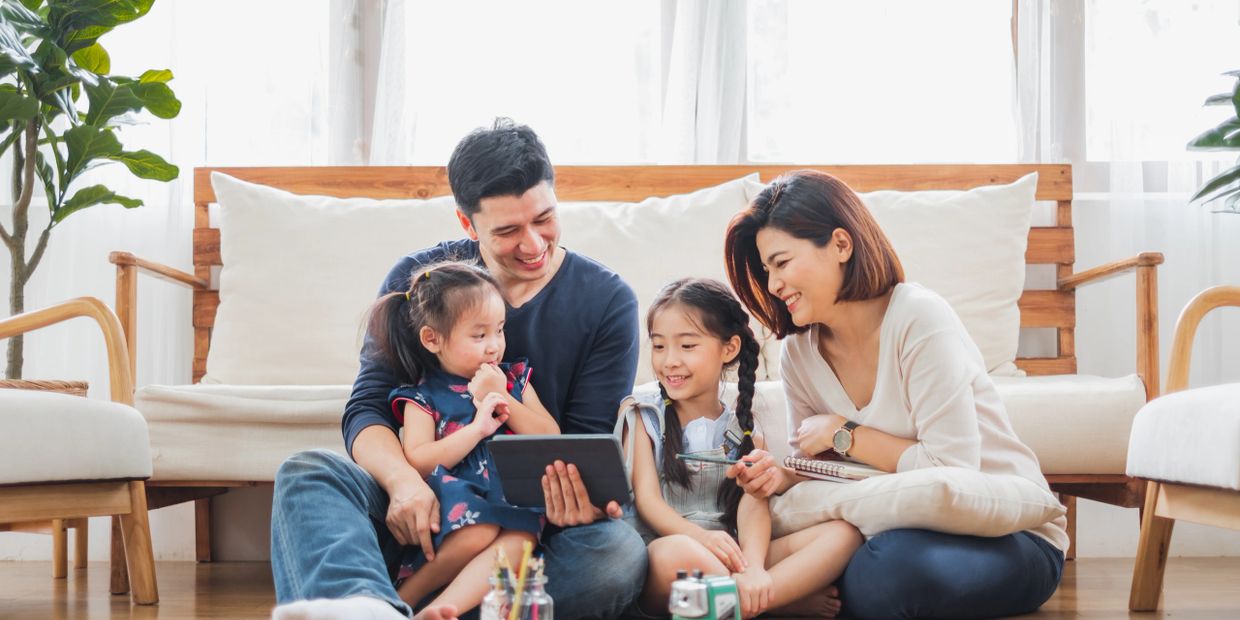 A happy family of four sitting on the floor, enjoying a tablet together.
