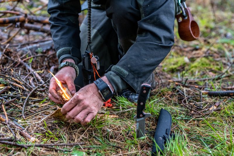 Close-up of man's hands igniting fire in forest.