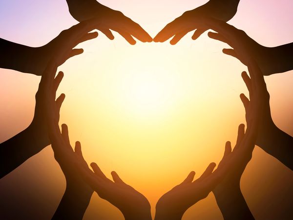 Multiple hands forming a heart shape against a sunset background.