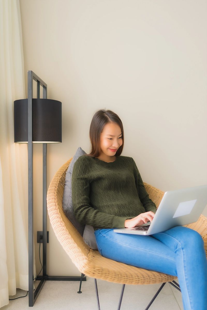 Portrait beautiful young asian women using computer or laptop for working and sitting on sofa chair in living room area
