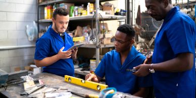 Three men in blue uniforms working and discussing in a workshop.
