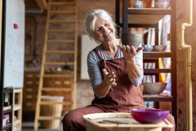 Elderly woman happily crafting pottery in a cozy studio.