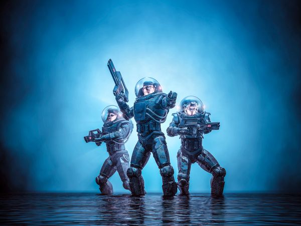 Three futuristic soldiers in armored space suits stand in water, ready for combat.