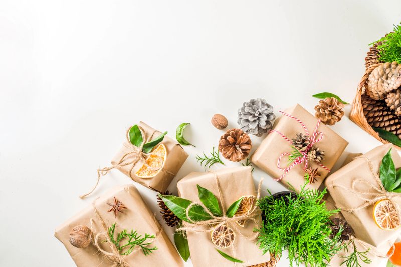 Zero waste christmas concept. Stack of handmade christmas gift boxes in craft paper with  different organic decoration and little live xmas tree in flowerpots.