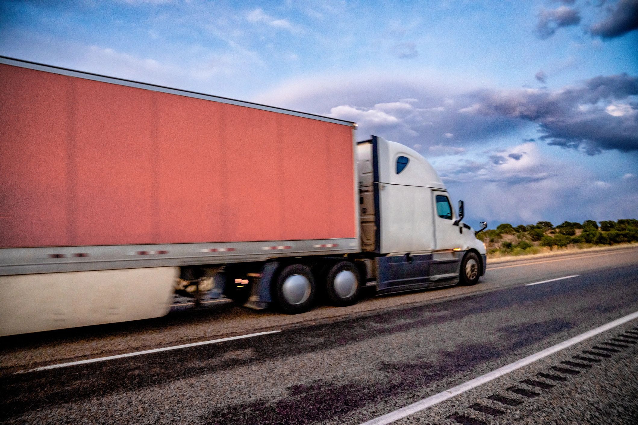 Semi truck with a red trailer driving on a highway