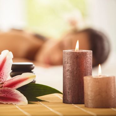 Spa setup with candles, flower, and essential oils, person relaxing in background.