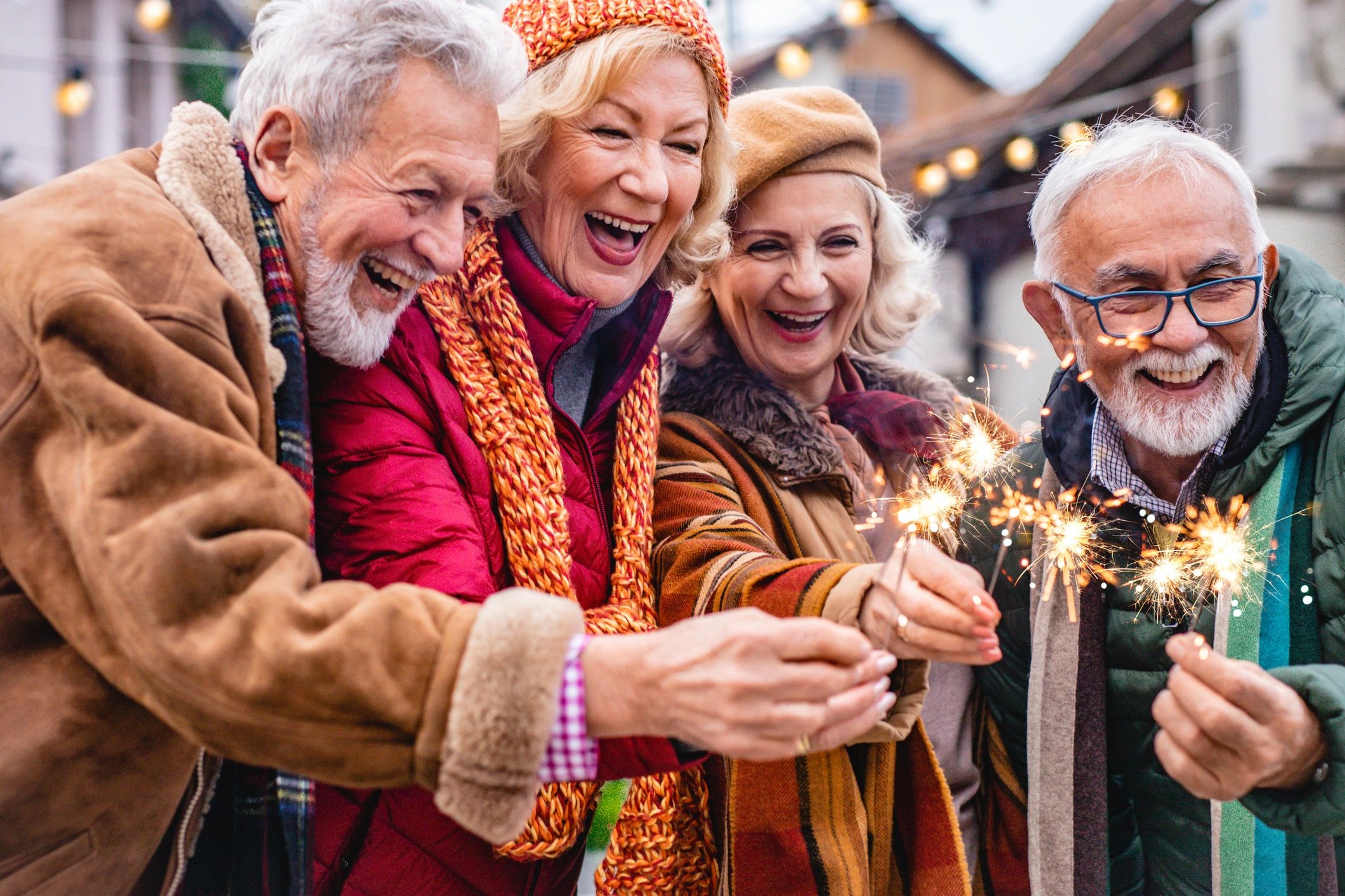 Four elderly friends joyfully holding sparklers outdoors in winter clothing.