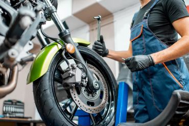 Mechanic working on a motorcycle front wheel with a wrench.