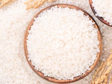 Close-up of white rice grains in wooden bowls with golden rice stalks.