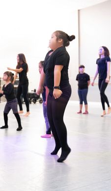 Children practicing dance moves in a studio wearing black outfits.