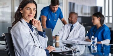 Confident female doctor with colleagues discussing in the background.