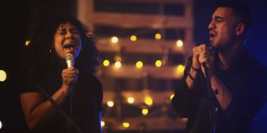 Two people singing into microphones on a dimly lit stage.