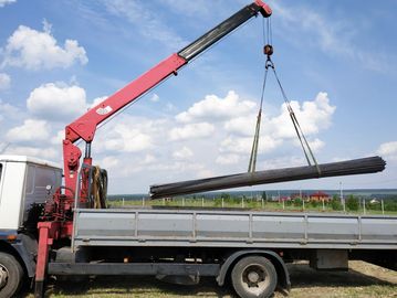 Truck with a red crane lifting steel rods under a blue sky.