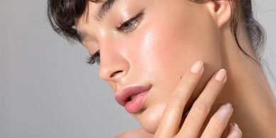 Close-up of a woman with flawless skin and manicured nails touching her face.