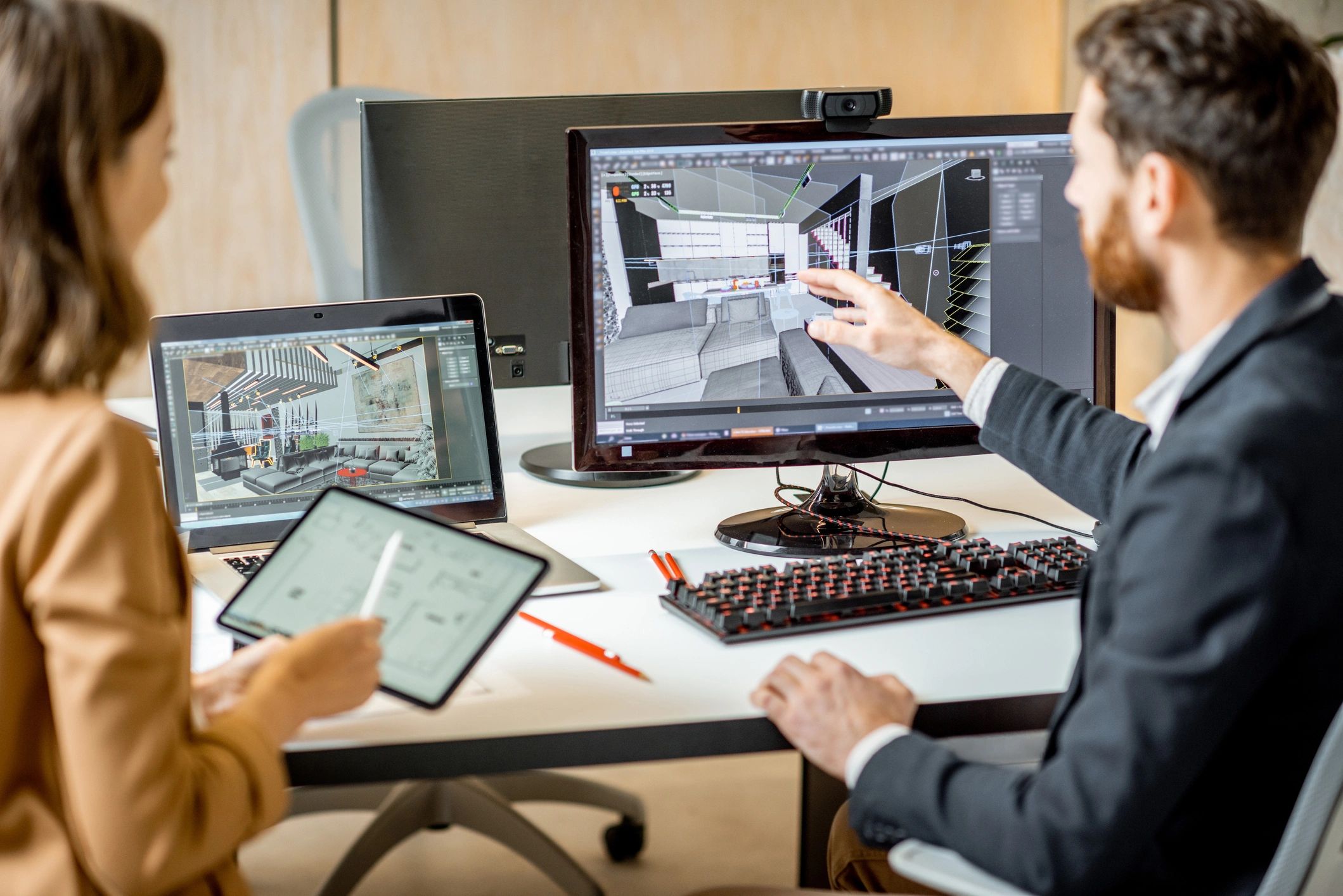 Two designers collaborating on 3D interior models at their desks.