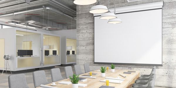 Modern meeting room with blank projector screen and wooden table.