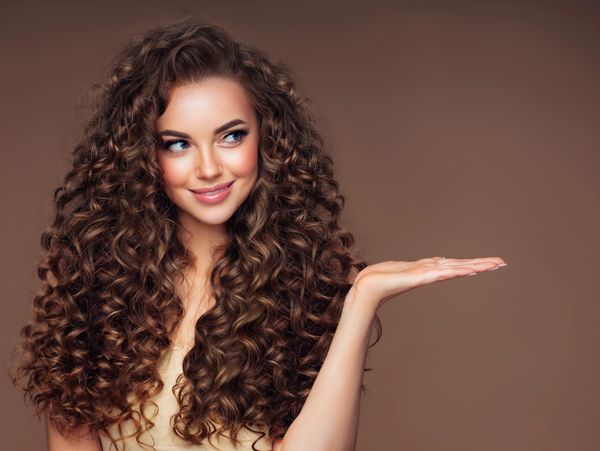 Smiling woman with long, curly hair holding her hand out against brown background.
