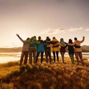 Group of friends embracing and enjoying a sunset by a lake.