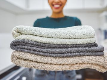 Person holding a stack of folded towels in neutral colors.