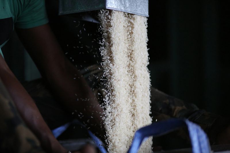 A Bangladeshi ethnicity male adult is holding bag near to machinery hose to fill in one tonne processed rice.