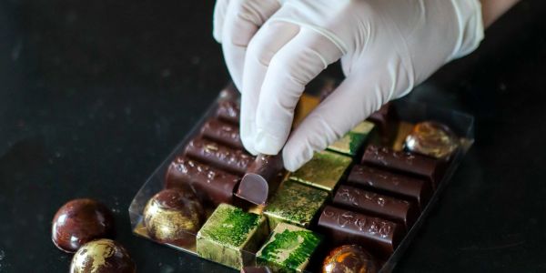Hand placing chocolate piece with gloves.