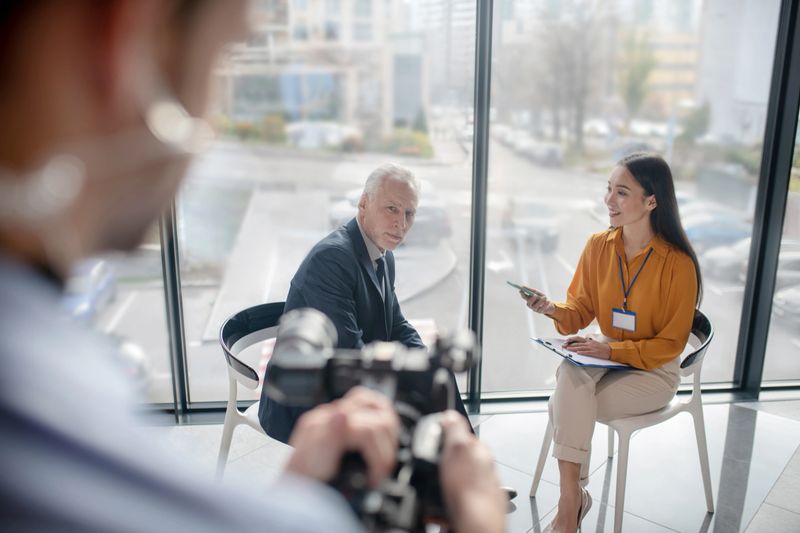 Work in progress. Asian female reporter siting in the studio interviewing a famous businessman