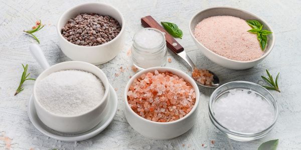 Various types of salt in bowls with herbs.