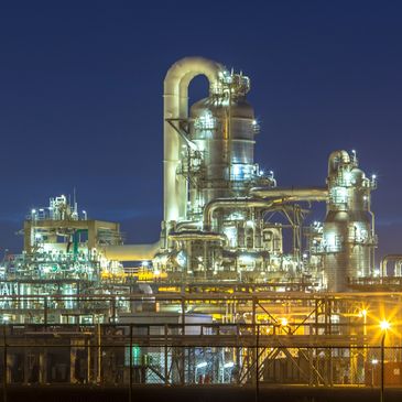 A brightly lit industrial refinery complex at night with metallic structures and pipes.