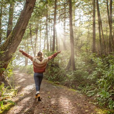 Person walking joyfully on a forest path with sunlight streaming through trees.