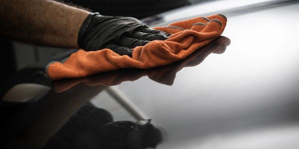 Person polishing a shiny black surface with an orange cloth.