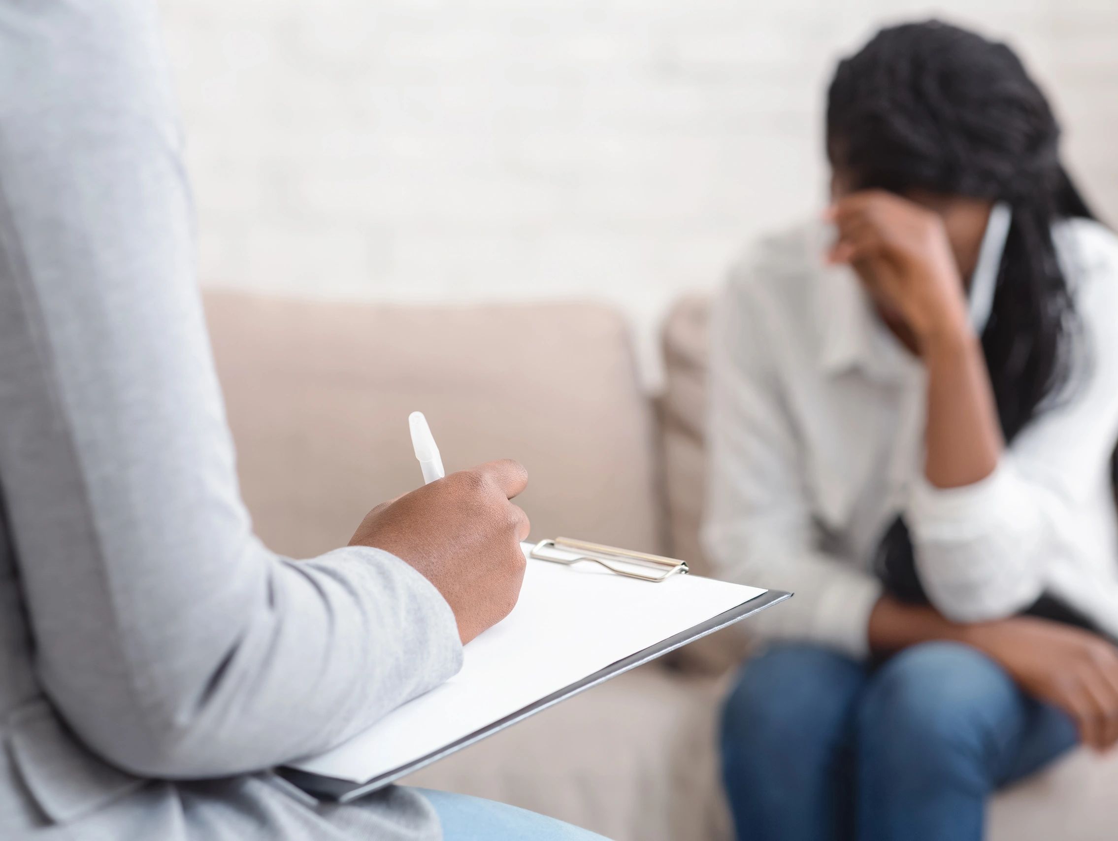 A therapist taking notes while a woman sits upset on a couch.