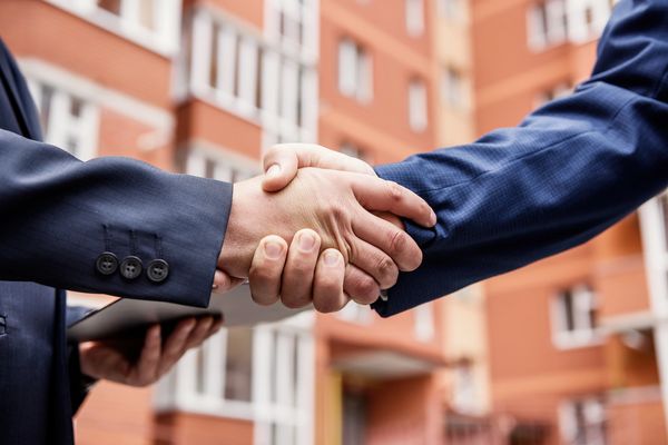 Two people shaking hands in front of a building.