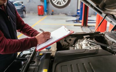 Mechanic inspecting car and writing notes on clipboard.