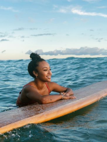 Woman smiling while resting on a surfboard in the ocean.
