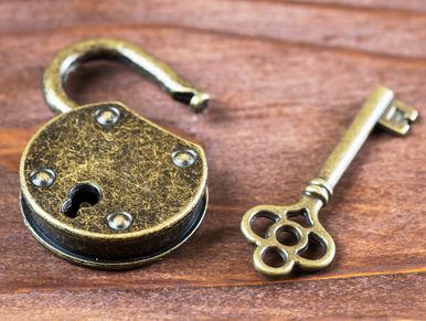 An antique brass padlock and its matching ornate key on wood.