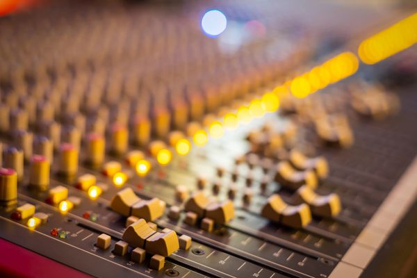Close-up of an audio mixing console with illuminated knobs and sliders.